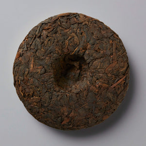 2023 DIGESTIF shou puer tea cake with dark compressed leaves and center depression on grey background