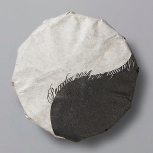 Round tea cake wrapped in black and white paper with "Paradox 2024" calligraphy design on top