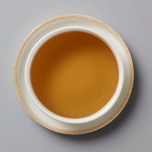 Cup of amber-colored NO SHADE white tea in ceramic vessel viewed from above on grey background