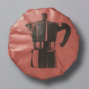 Round wrapped shou pu’er tea cake with moka pot illustration on rust-colored paper wrapping
