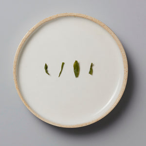 Sonogi Tama green tea leaves arranged on white ceramic plate showing different cultivar leaf shapes and textures