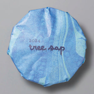 Round blue package of Tree Sap 2024 black tea wrapped in patterned paper on gray background