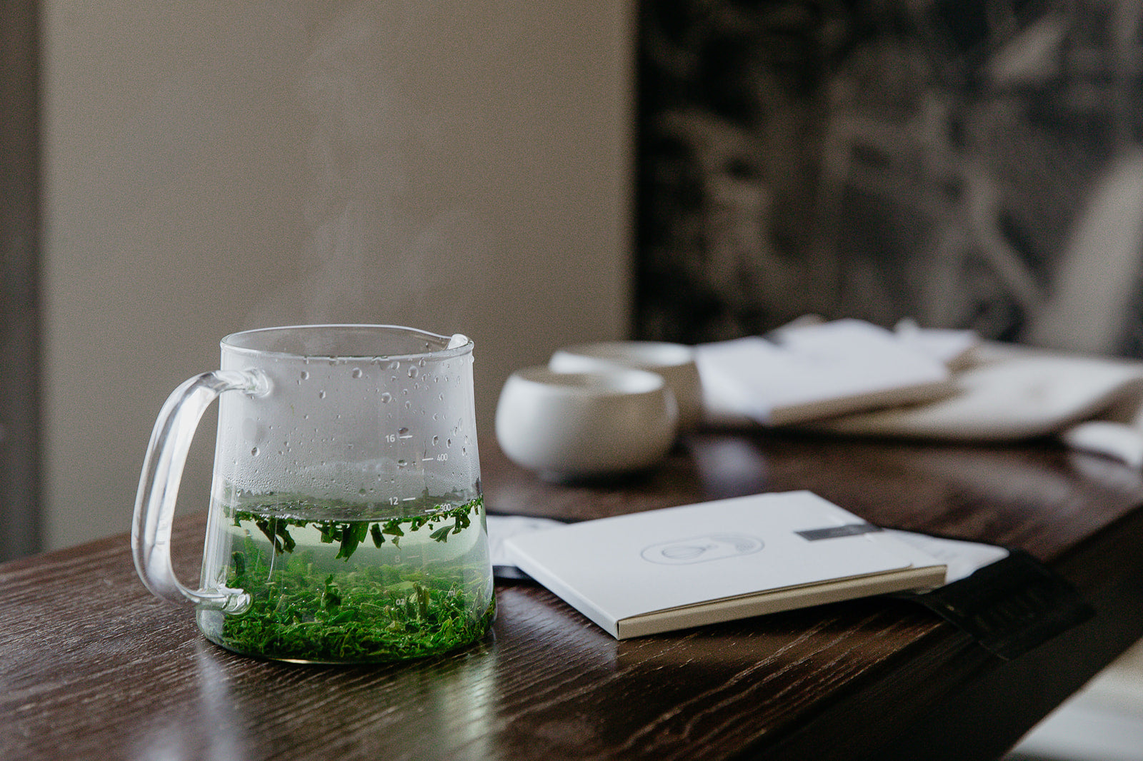 Glass teapot with green tea on a wooden table.