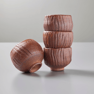 Four ceramic red teacups stacked on grey background