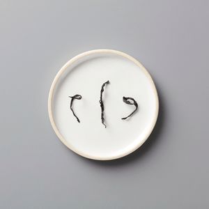 PANLAN 105 yancha oolong tea leaves displayed on white ceramic plate, showing twisted dark strands against plain background