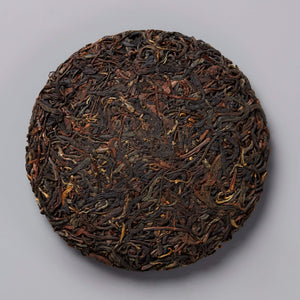 2020 BRUISER black tea cake, compressed dark leaves with golden tips in circular disc form on gray background