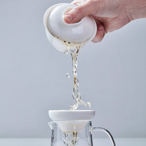 BOLI MINI white glass teapot pouring water into clear glass pitcher with splash effect on gray background