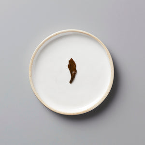 LINS RED black tea leaf on white ceramic plate with beige rim, showcasing single oxidized leaf