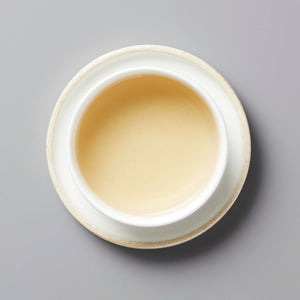 RAWISM sheng puer tea in white ceramic cup showing golden amber liquor against grey background