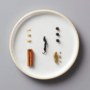 Masala Chai Concentrate spices displayed on white ceramic plate including cinnamon, peppercorns, cardamom and ginger