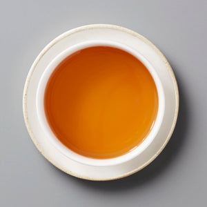 Champagne Long Kou oolong tea with amber-colored liquor in white ceramic cup on grey background