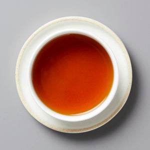 Brewed 2020 Digestif shou puer tea in white ceramic cup showing rich amber-red liquor against grey background