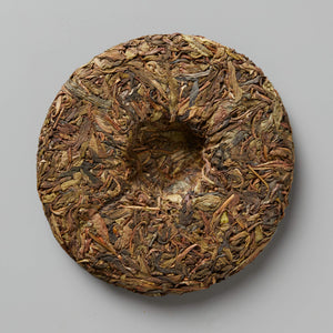 Compressed disc of Grandpas Flask huangpian sheng puer tea showing aged brown leaves and traditional cake shape