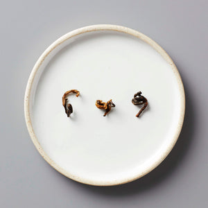 HUGO GREY black blend tea leaves artfully arranged on white ceramic plate showing natural curl and texture