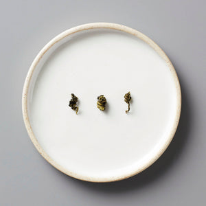GUI SHAN oolong tea leaves arranged on a white ceramic plate, showing rolled dark green leaves against minimalist backdrop