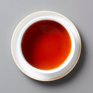 Rich amber-red INK JET shou puer tea liquor in white ceramic cup with beige rim on grey background