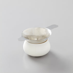 Steel filter resting on white ceramic vessel, designed for straining tea leaves during traditional gongfu tea preparation