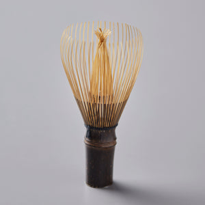 Chasen Tanimura handcrafted bamboo matcha whisk with delicate golden tines and dark brown handle on gray background