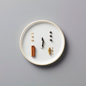 Vanilla Chai black tea blend ingredients on white ceramic plate showcasing cinnamon, black tea leaves and spices