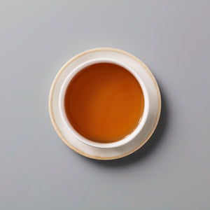 Zi Ran Smoke black tea in white ceramic cup showing rich amber-colored liquor on grey background
