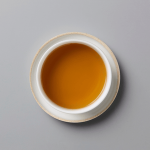 A top-down view of a white ceramic cup filled with amber-colored tea, set against a solid gray background.