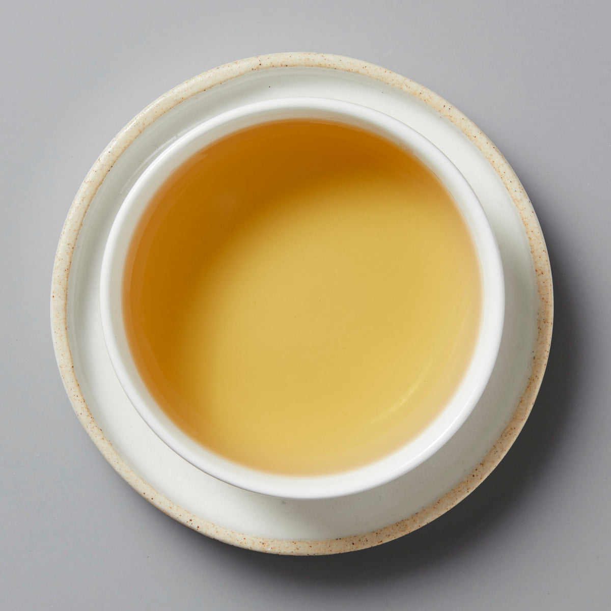 Top-down view of light golden Florist 2024 white tea in a white ceramic cup and saucer on gray background