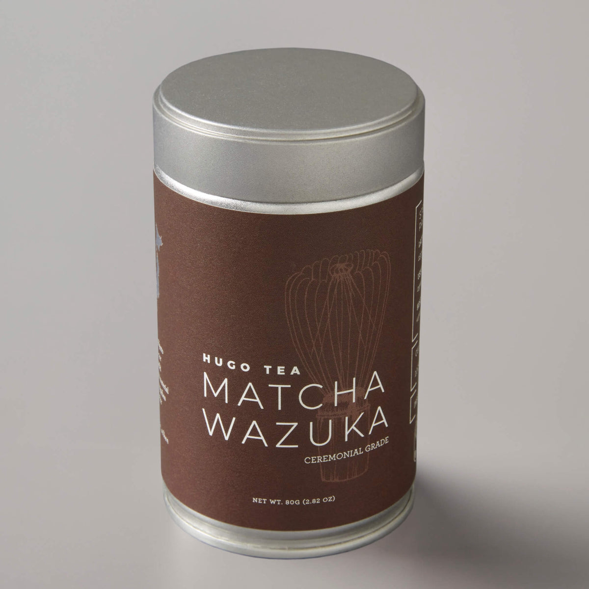 Matcha Wazuka ceremonial grade tea in cylindrical silver tin with brown label featuring minimalist whisk design