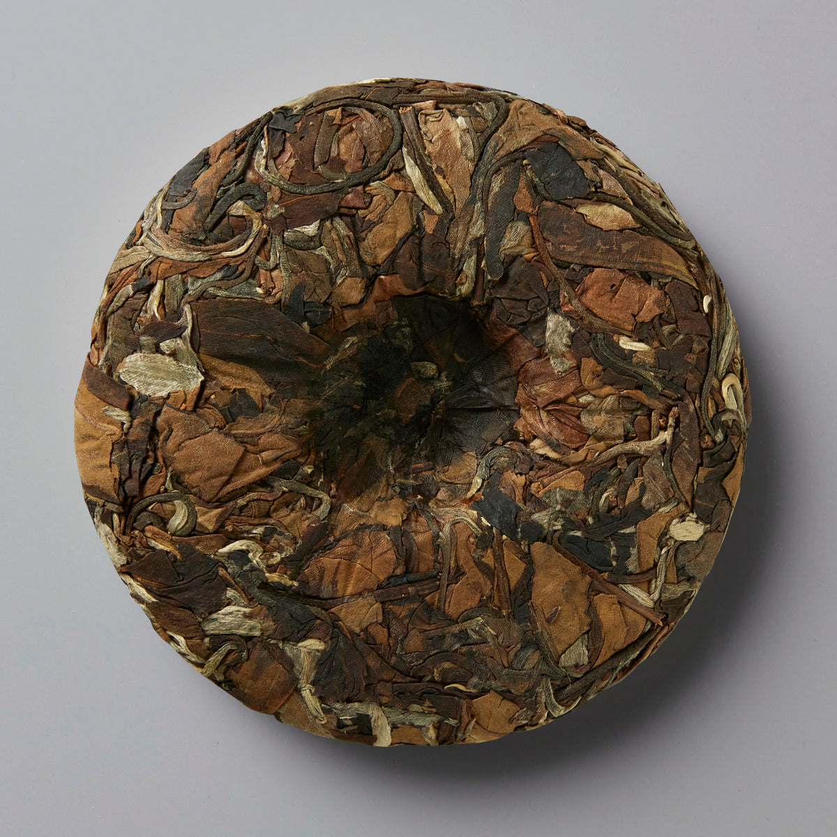 NOT FROM CONCENTRATE white tea cake disc showing compressed brown and golden tea leaves in circular pattern