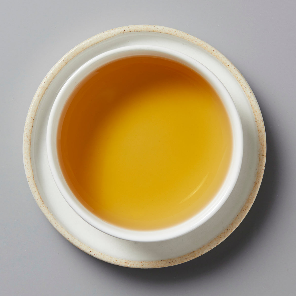 Top view of a white cup filled with clear coppery-yellow Paradox 2024 black and white tea on a matching saucer.