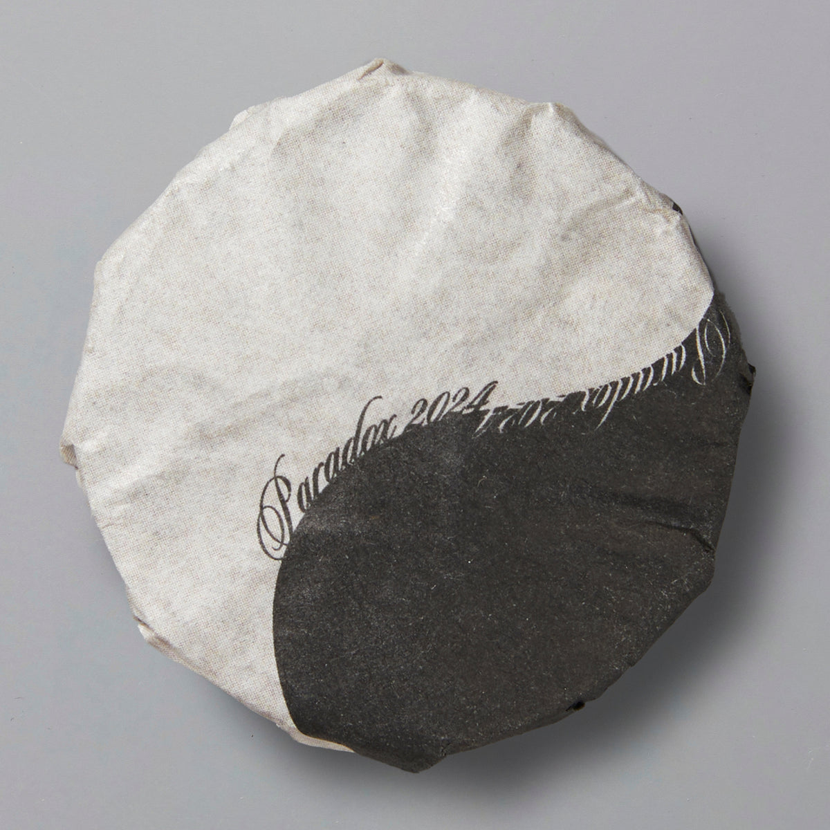 Round tea cake wrapped in black and white paper with "Paradox 2024" calligraphy design on top