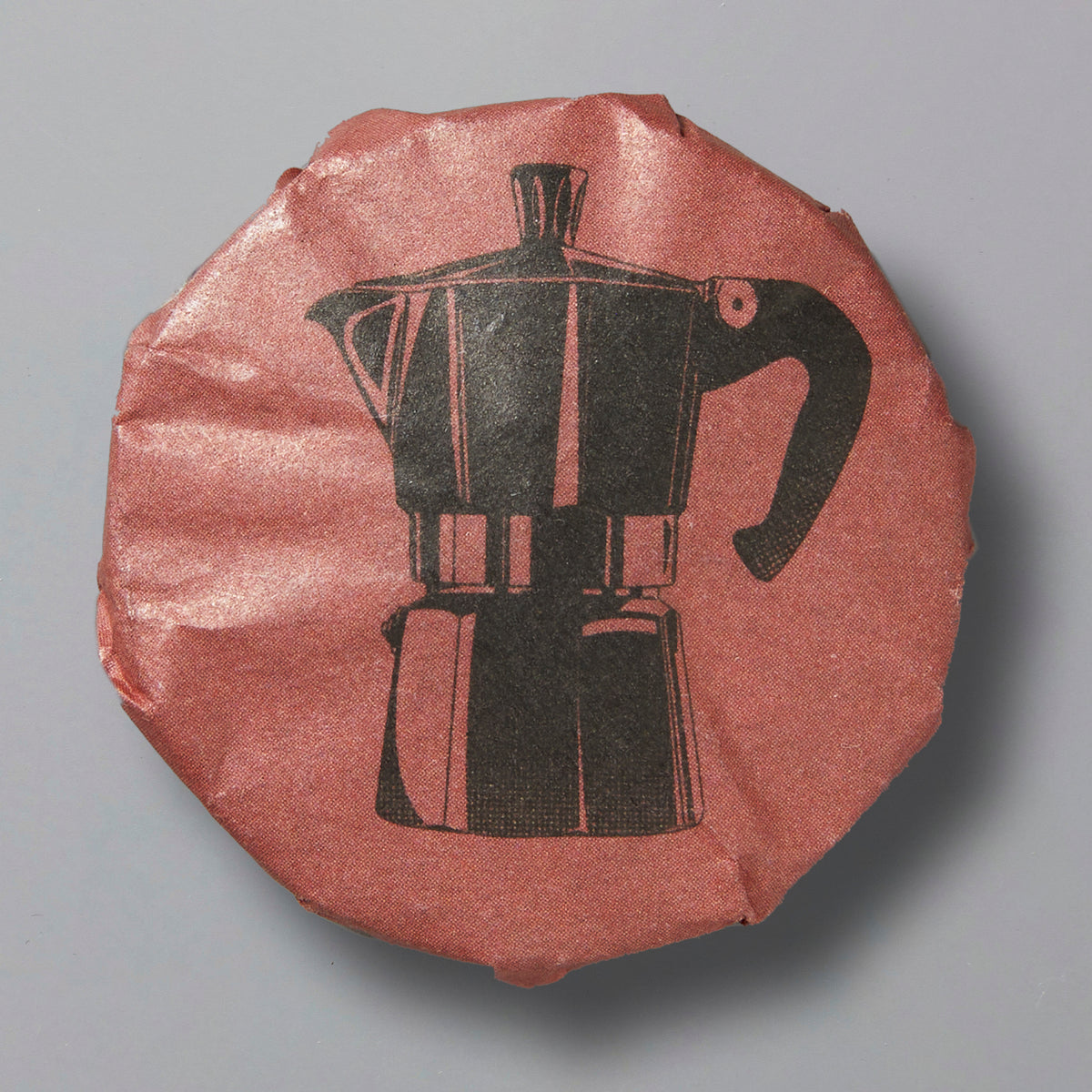 Round wrapped shou pu’er tea cake with moka pot illustration on rust-colored paper wrapping