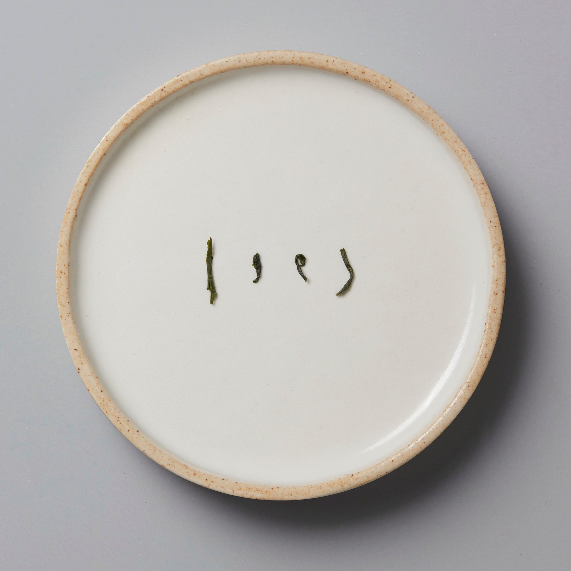 SONOGI TAMA green tea leaves arranged artistically on a white ceramic plate with beige rim, showing tea's natural curl