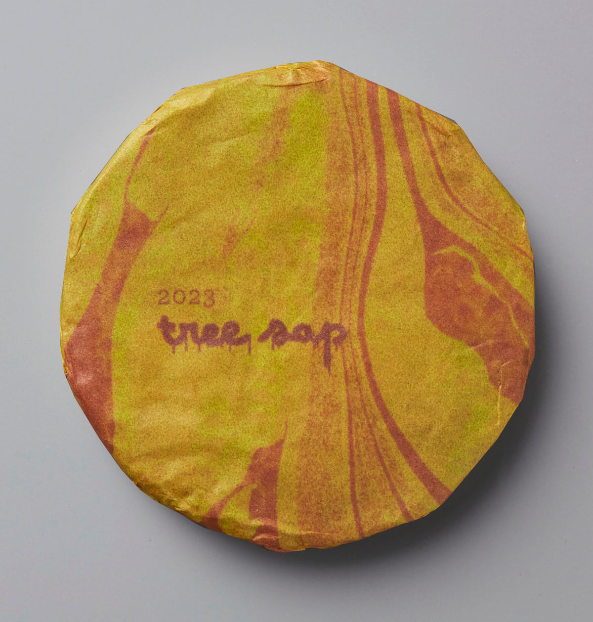 2023 Tree Sap black tea cake with yellow and orange marbled wrapping paper showing handwritten text on circular compressed tea