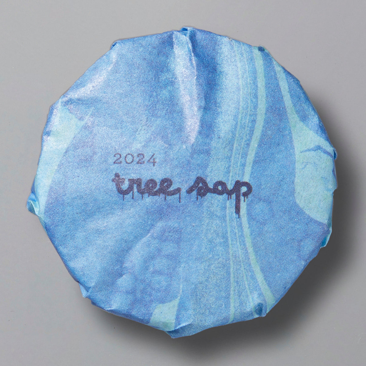 Round blue package of Tree Sap 2024 black tea wrapped in patterned paper on gray background