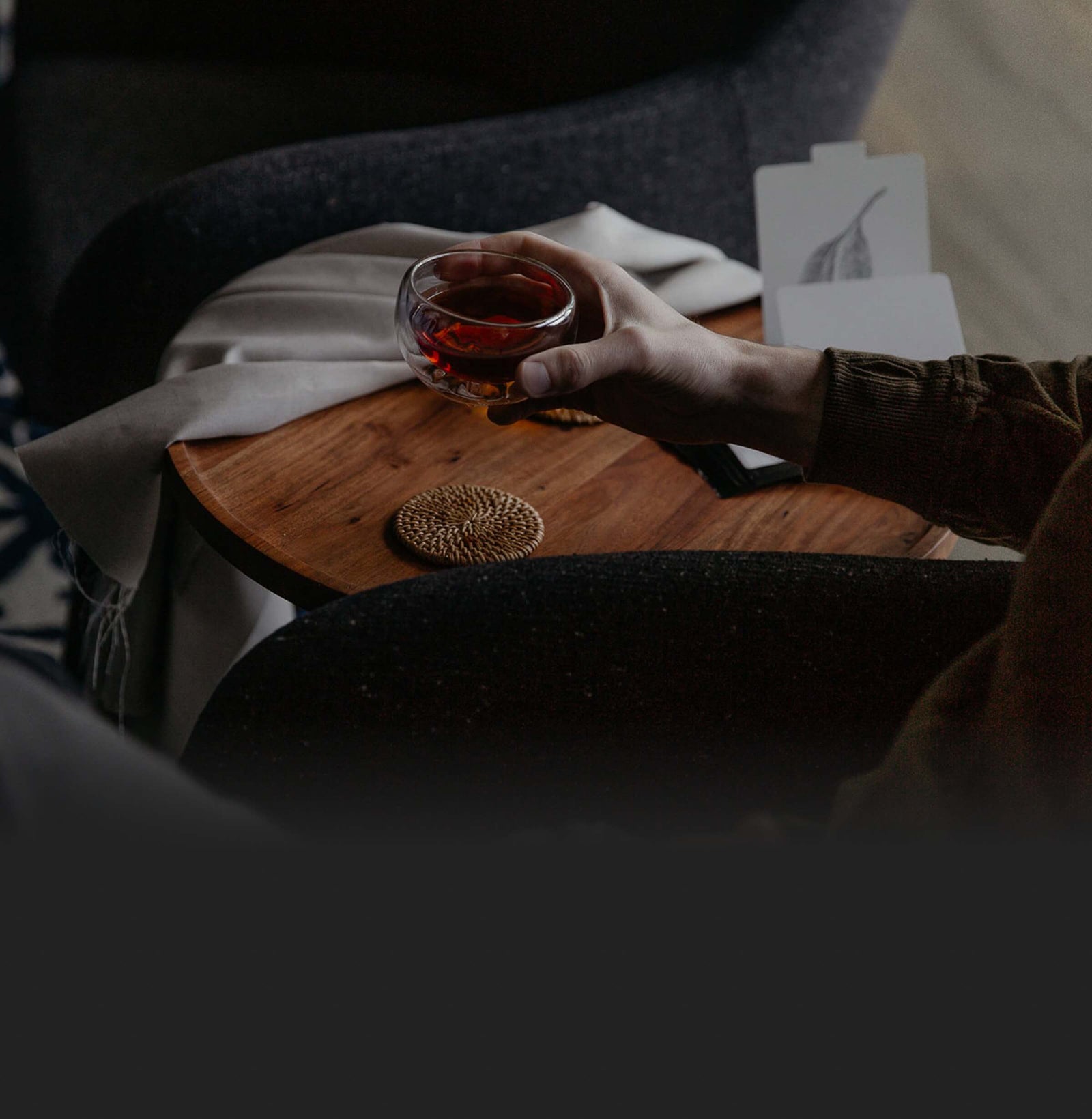 Hand holding a glass cup of tea over a wooden table in a calm, dim setting.