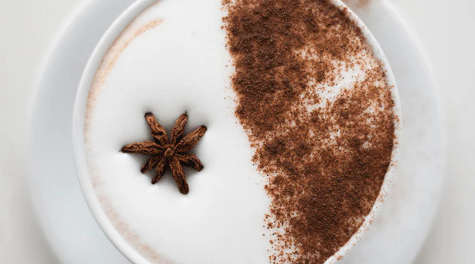 A creamy chai latte in a white cup, topped with a light dusting of cocoa powder on one side and a star anise on the other, exuding a cozy, warm feel.