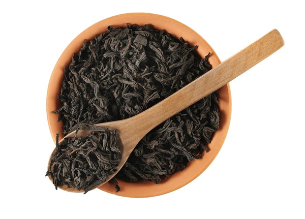 Close-up of loose leaf oolong tea in a terracotta bowl with a wooden spoon, showing dark, twisted tea leaves for a product or brewing concept.