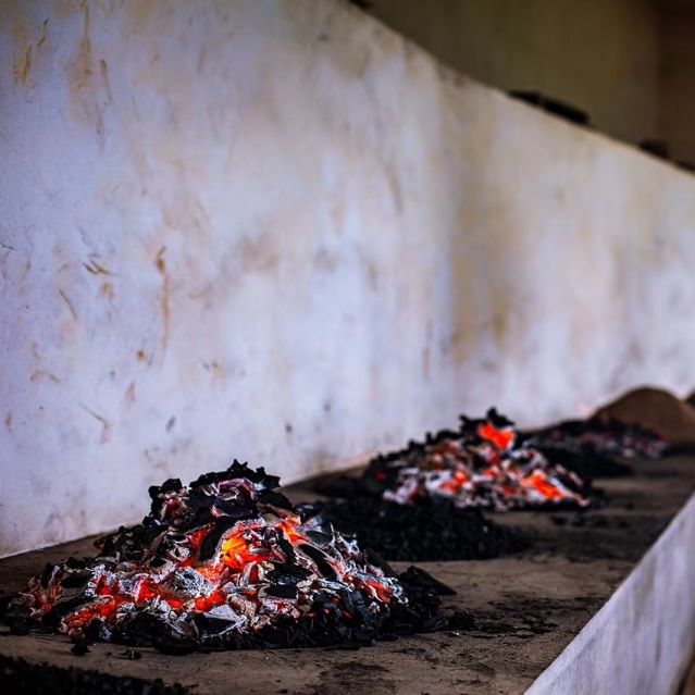 Small mounds of glowing embers on a concrete surface line up against a stained white wall, creating a warm, rustic atmosphere.