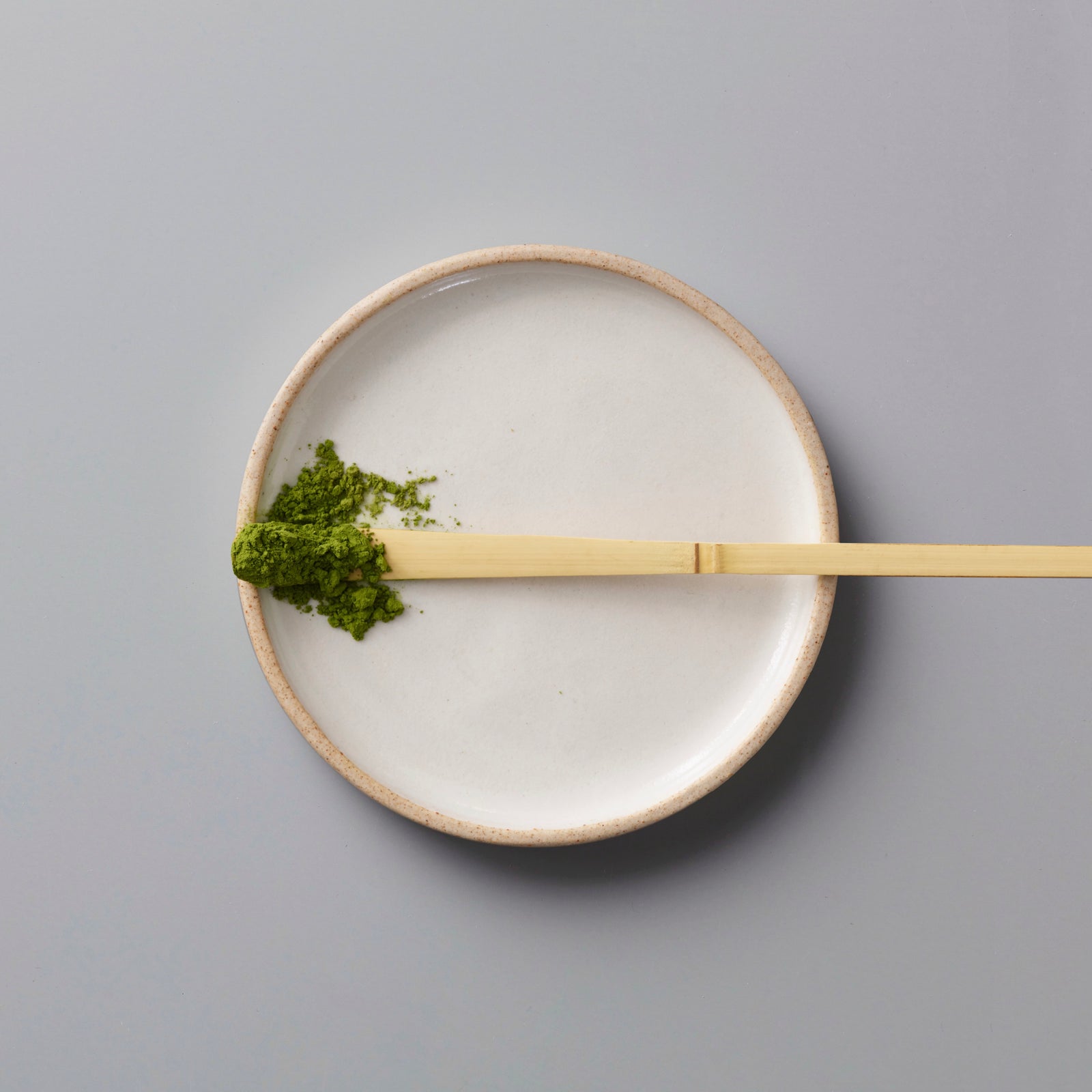 Ceremonial grade MATCHA ANSHUN vibrant green powder on bamboo scoop, placed on minimalist ceramic plate.