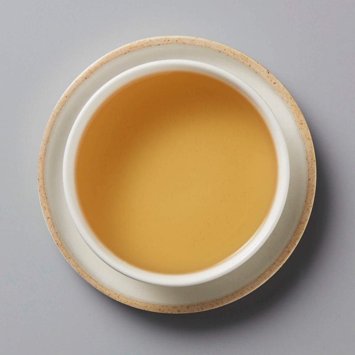 Grandpas Pocket huangpian sheng puer tea in white ceramic cup showing golden amber colored liquid on gray background
