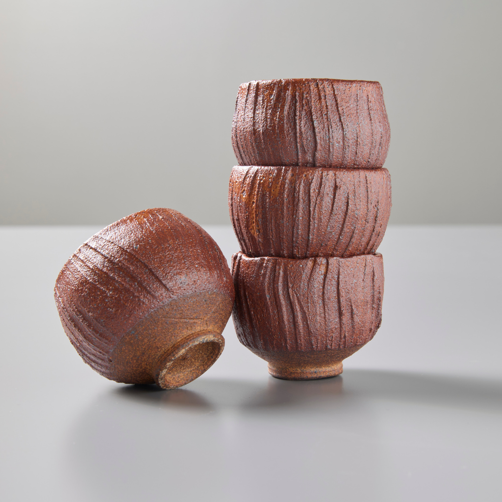 Four ceramic red teacups stacked on grey background