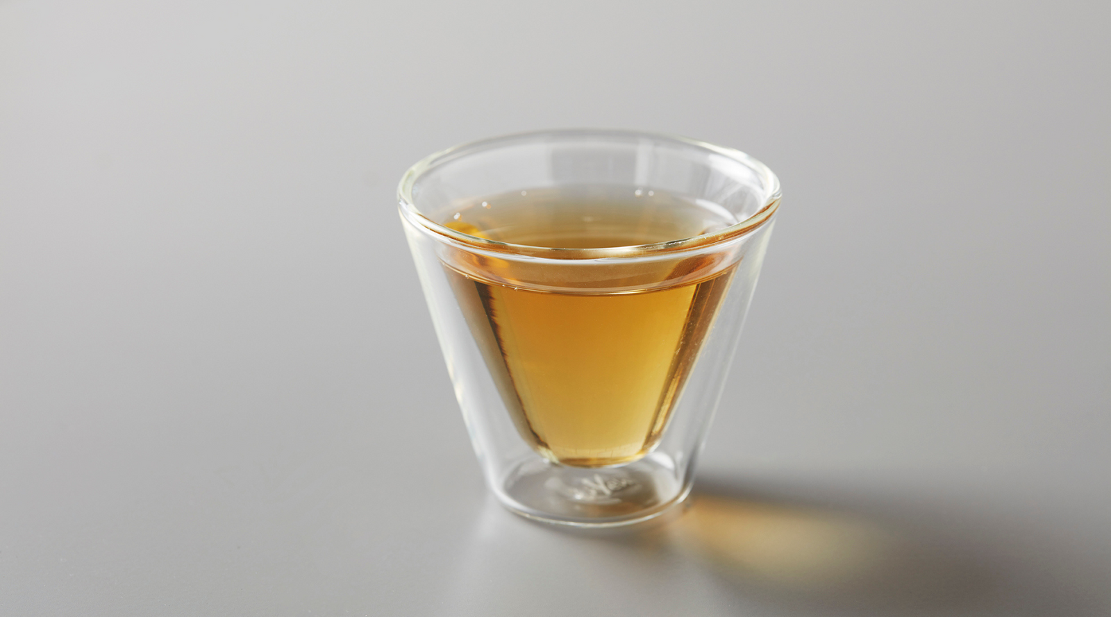 Clear glass cup with amber tea liquid on a gray background