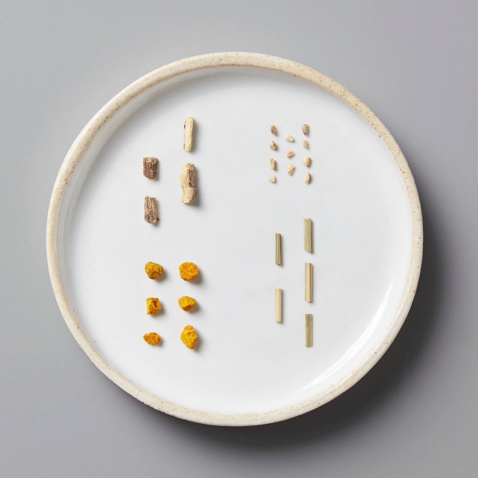 GOLD tisane blend ingredients displayed on white ceramic plate showing turmeric, ginger, licorice root and lemongrass pieces