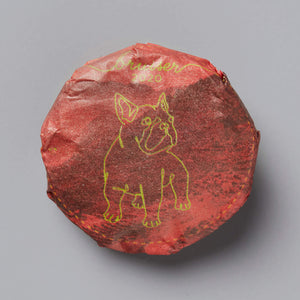 2020 BRUISER black tea cake with gold dog illustration on red wrapping paper against grey background
