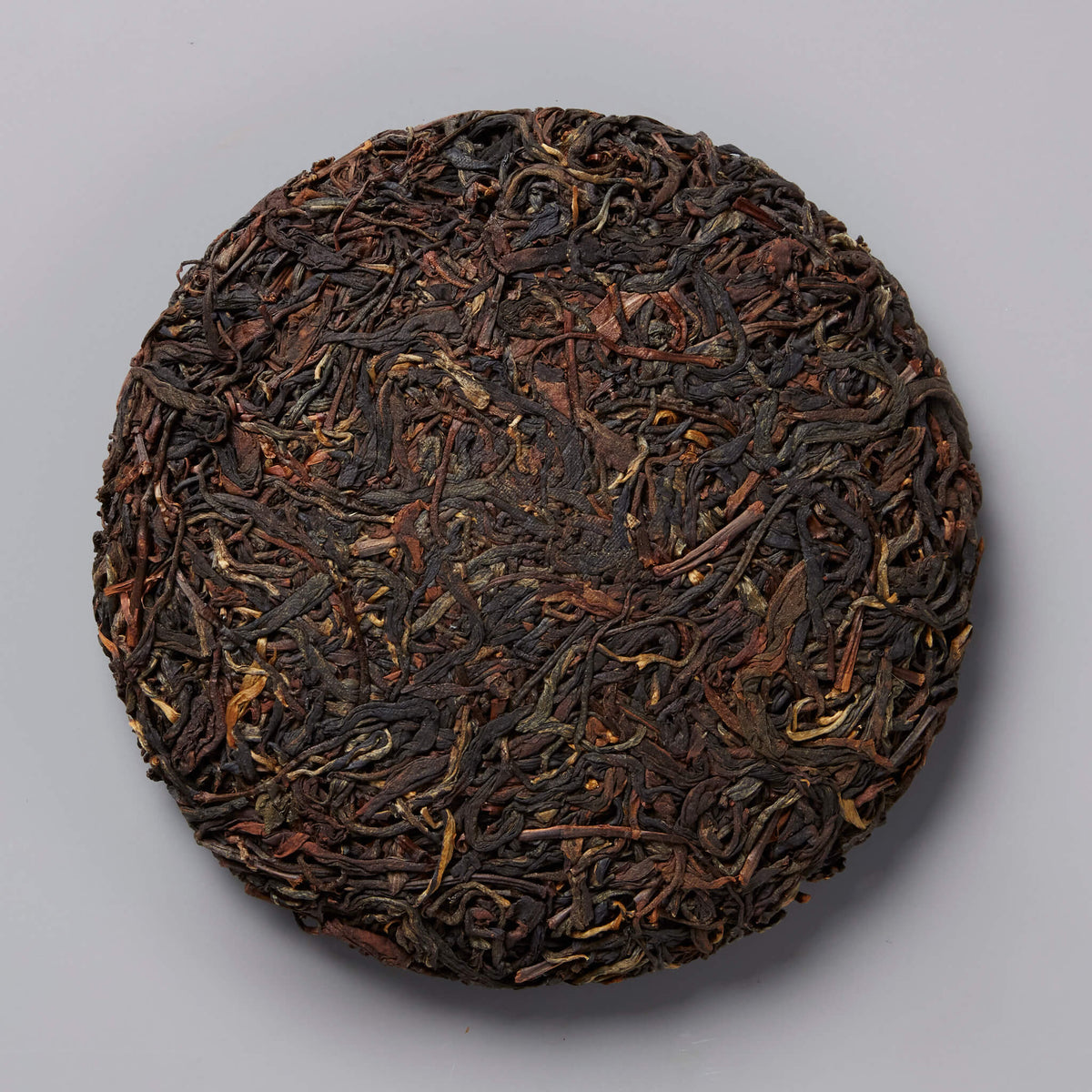 2020 BRUISER black tea cake, compressed dark leaves with golden tips in circular disc form on gray background