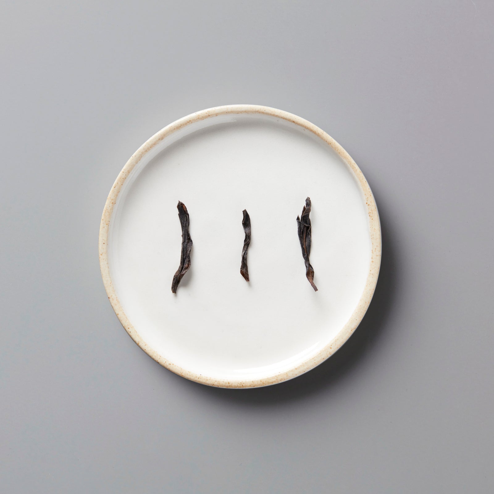 Three twisted dark tea leaves of LINS DUCK dancong oolong arranged on a white ceramic plate with beige rim