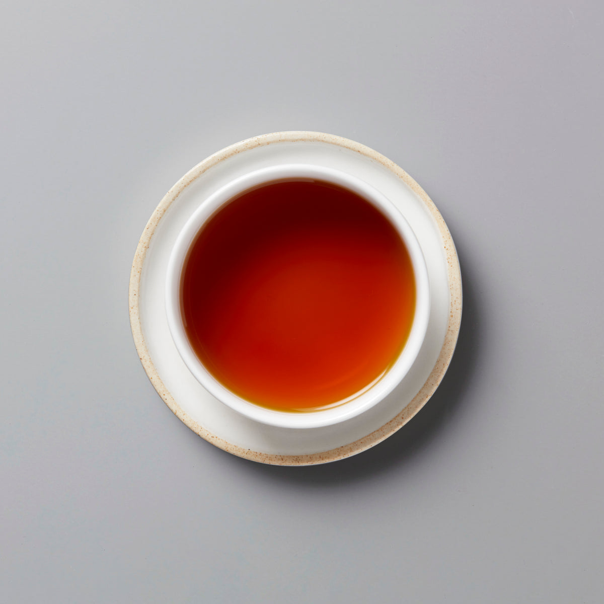 LINS RED black tea in white ceramic cup showing rich amber-red liquor against grey background