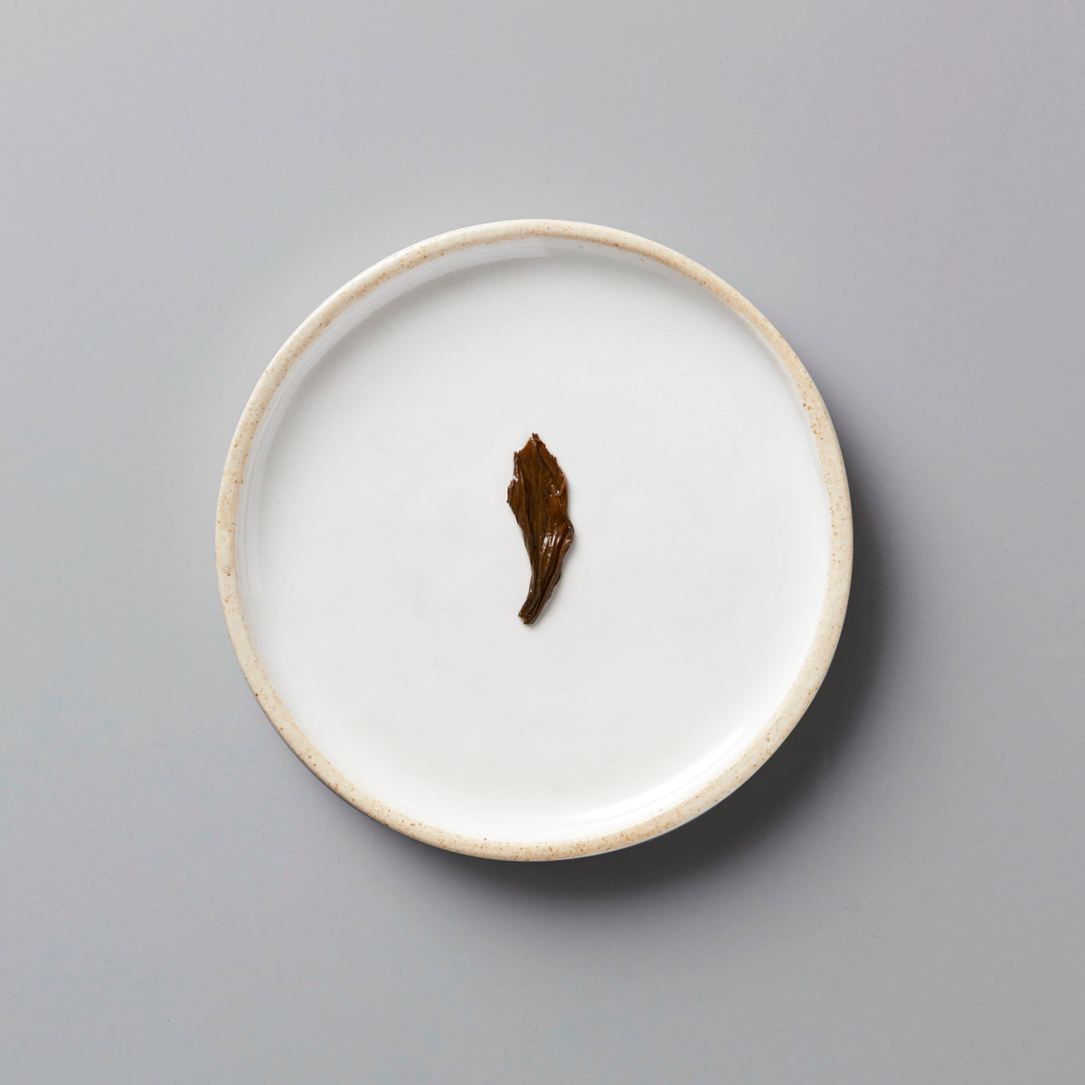 LINS RED black tea leaf on white ceramic plate with beige rim, showcasing single oxidized leaf