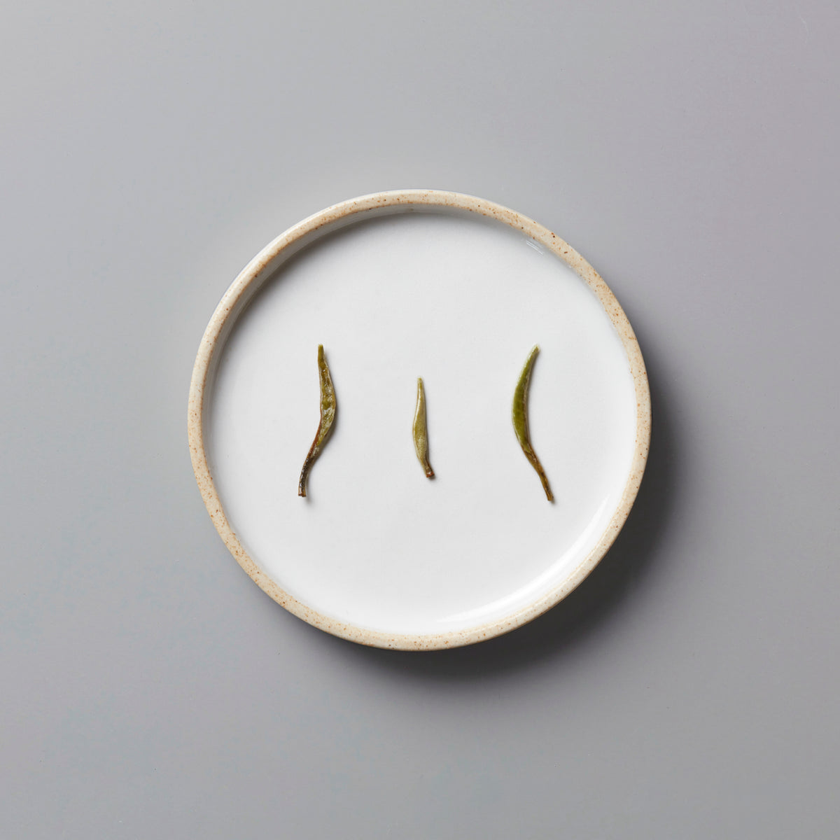 Ma Wei Needles white tea buds displayed on white ceramic plate showing three delicate silver needle tea leaves