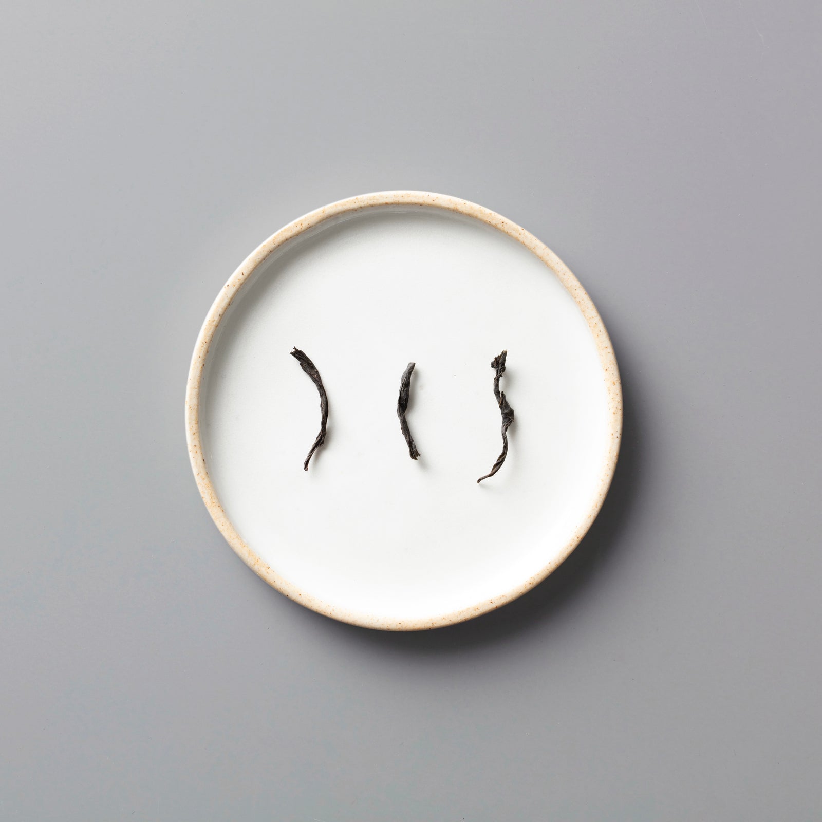 Three twisted Panlan Que She yancha oolong tea leaves arranged on a minimalist white ceramic plate